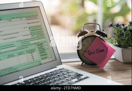 tax time post-it on alarm clock and Individual income tax return form online. Stock Photo