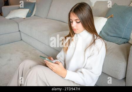 Portrait of a gorgeous young woman using her smartphone and smiling while sitting on the floor at home Stock Photo