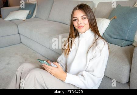 Portrait of a gorgeous young woman using her smartphone and smiling while sitting on the floor at home Stock Photo