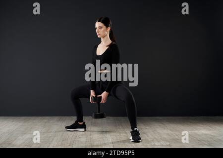 Sporty young woman doing squats with dumbbell during crossfit. Stock Photo