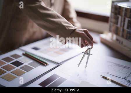 Female architect using divider compass to drawing building project and design interior on blueprint. Stock Photo