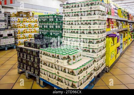 Italy - December 15, 2023: Cans of blonde lager beer of various types in boxes of various brands stacked on pallets for sale in Italian supermarket Stock Photo