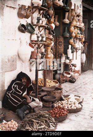 Tunis, Tunisia A fruit and vegetable seller in front of a pottery shop in a souk in the medina, Economic activity, Clothing, Daily life, Sciences, Techniques, Nature, Environment, Human beings, Shop, store, Costume, Market, fair, Small trade, Food, Measuring instrument, Street scene, Domestic object, Vegetable, Ceramics, Vegetation, botany, Man, Tunis, Pottery merchant, Médina de Tunis, 01/01/1911 - 31/12/1911, 01/01/1910 - 31/12/1910, 01/01/1909 - 31/12/1909, Gervais-Courtellemont, Jules, 1909 ou 1910 - Algérie, Tunisie - Jules Gervais-Courtellemont et Souvieux, Autochrome, photo, Glass, Auto Stock Photo