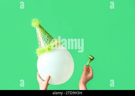 Female hands with balloon in party hat and whistle on green background. Birthday celebration Stock Photo