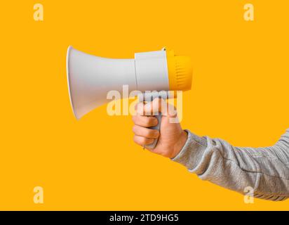 Young man with megaphone on yellow background Stock Photo