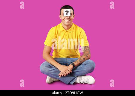 Young man with paper question mark on his forehead against purple background Stock Photo