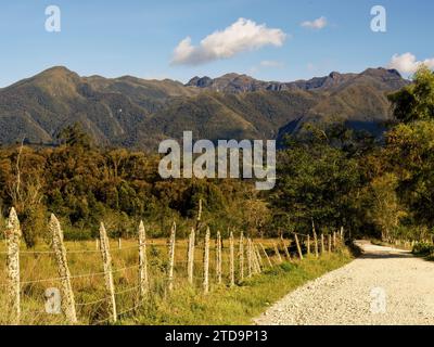 A gravel rural road flanked by the barbed wired fences of farmlands, in a clear afternoon, in the eastern Andean mountains of central Colombia. Stock Photo