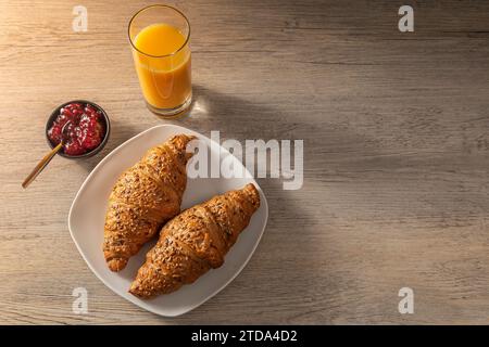 Breakfast. Orange juice, raspberry jam, and croissants on  a white plate. Top view on wooden table. Stock Photo