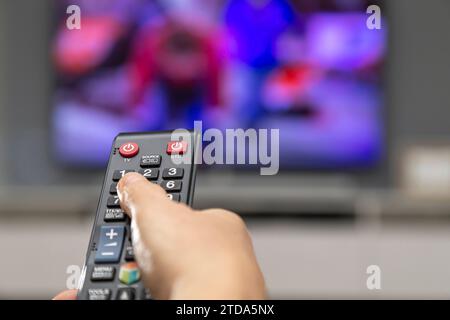 A woman's hand with a remote control switches channels on the TV. Stock Photo