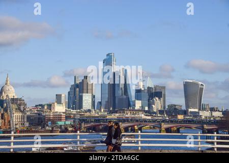 People walk along Waterloo Bridge past the City of London skyline, the capital's financial district, on a sunny and mild day. Stock Photo