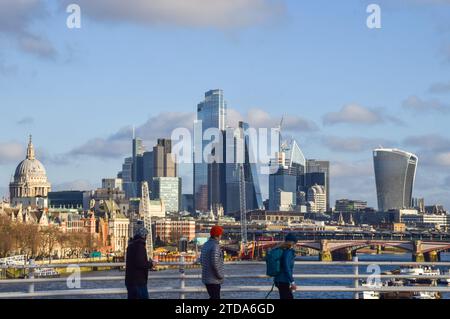 People walk along Waterloo Bridge past the City of London skyline, the capital's financial district, on a sunny and mild day. Stock Photo