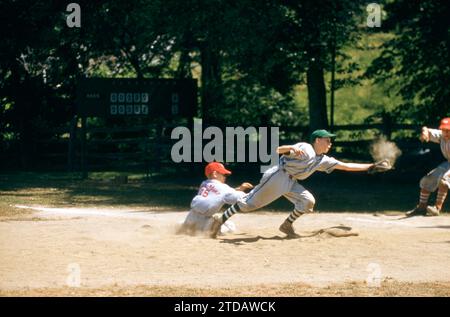 KINGS POINT, NY - 1960'S:  General view of a child sliding back to the base as the first baseman tries to catch the ball during a game between two teams from Kings Point Little League circa 1960's in Kings Point, New York.  (Photo by Hy Peskin/Getty Images) Stock Photo