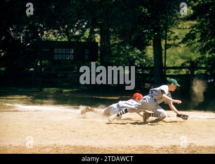 KINGS POINT, NY - 1960'S:  General view of a child sliding back to the base as the first baseman tries to catch the ball during a game between two teams from Kings Point Little League circa 1960's in Kings Point, New York.  (Photo by Hy Peskin/Getty Images) Stock Photo