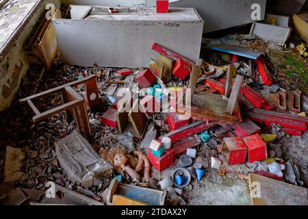 A cluttered room with scattered toys, wooden blocks, a doll, and debris on the floor. The area looks abandoned and in disarray. Scattered furniture an Stock Photo