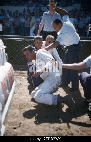 SACRAMENTO, CA - AUGUST, 1958: A group of men tend to the driver after his car flipped and crashed during a car show at the Sacramento State Fair circa August, 1958 in Sacramento, California. (Photo by Hy Peskin) Stock Photo