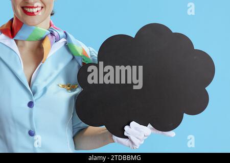 Closeup on smiling female flight attendant on blue background in blue uniform showing blank cloud shape board. Stock Photo