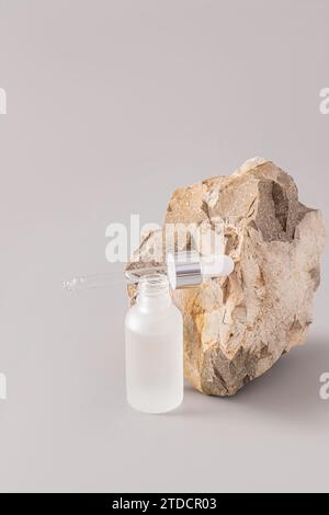 An open matte bottle with a cosmetic anti aging moisturizer and a pipette filled with it lies on the bottle. natural stone. Vertical grey view Stock Photo