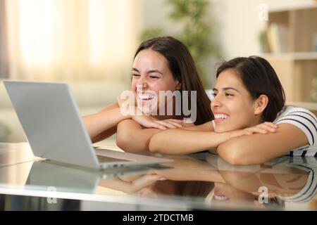 Two happy women laughing watching media on laptop at home Stock Photo