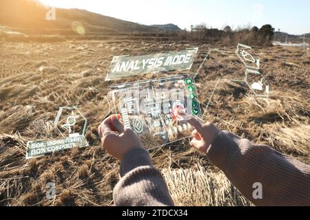 In the harvested winter rice paddies, a woman is using an AR device to analyze the soil and progress (hologram and CG effects are applied) Stock Photo