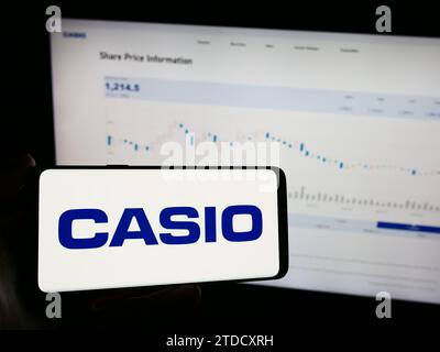 Person holding mobile phone with logo of Japanese electronics company Casio Computer Co. Ltd. in front of web page. Focus on phone display. Stock Photo