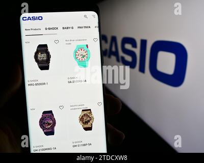 Person holding cellphone with web page of Japanese electronics company Casio Computer Co. Ltd. in front of logo. Focus on center of phone display. Stock Photo