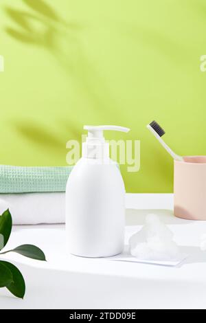 Front view of an unlabeled bottle of shower gel, next to white foam, two folded towels, a toothbrush and a ceramic cup. Simulate bathroom space. Stock Photo