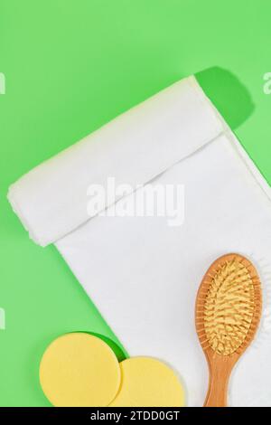 A detangling comb, a white towel and two yellow sponges are displayed on a green background. Ideal space for advertising body care products such as sh Stock Photo