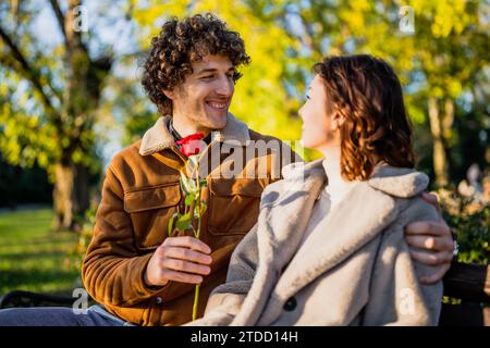 Portrait of happy loving couple in park. Man is giving rose to his woman. Stock Photo