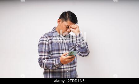 Young Asian man holding his mobile phone with sad and Confused expression on white background. studio shot Stock Photo