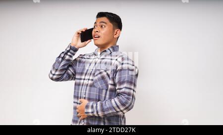 Asian young man using smartphone with shocked and surprised face expression. talk on smartphone. studio shot Stock Photo