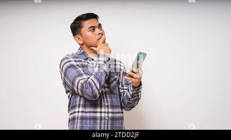 Young Asian man holding his mobile phone with sad and Confused expression on white background. studio shot Stock Photo