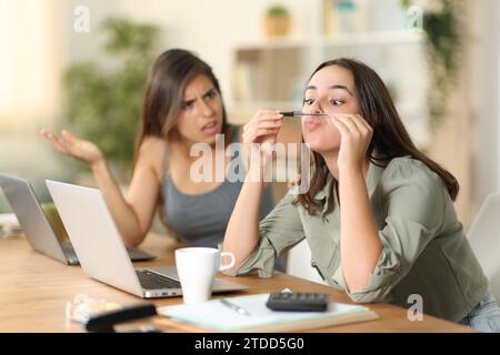 Angry tele worker scolding to her lazy colleague who is wasting time at home Stock Photo