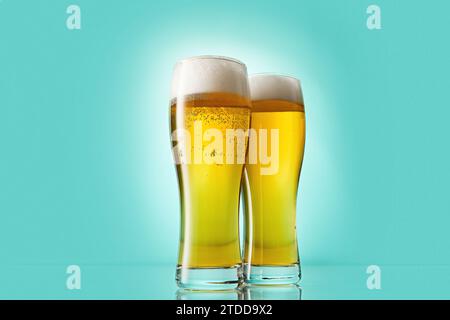 Fizzy yellow beer poured to tall glasses on light blue. Stock Photo