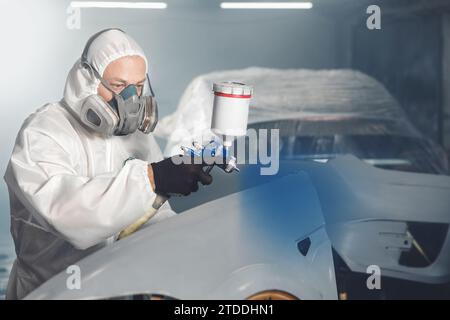 Car paint worker spraying blue paint to car body element using spray ...