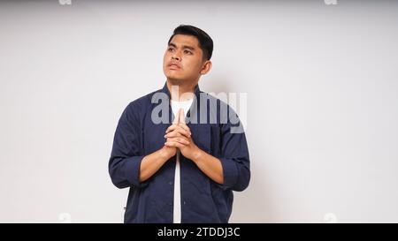 Young Asian man showing thinking gesture with his eyes looking up on white background. studio shot Stock Photo