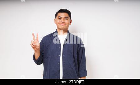 Young Asian man showing happy face expression while giving two fingers sign Stock Photo