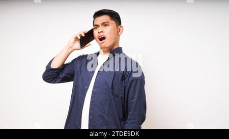 Asian young man using smartphone with shocked and surprised face expression. talk on smartphone. studio shot Stock Photo