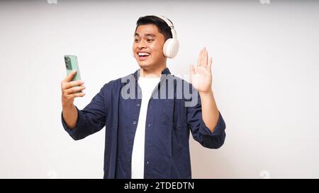 Happy young Asian man wearing wireless headphones listening to music from smartphone studio shot isolated on white background Stock Photo