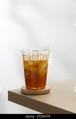 Iced tea in a clear plastic glass on a wooden table with a white background. Stock Photo