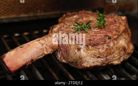 Cooking a rib-eye steak on a grill, griller or bbq. A large rib eye with bone-in sizzling away of a barbecue with flame or flare-up. Beef meat concept Stock Photo