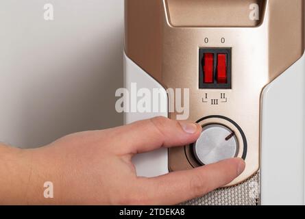 A man's hand regulates the heating power of an electric air heater in an apartment, close-up. Copy space for text Stock Photo