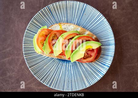 a birds eye view over a slice of white bread toast topped with sliced tomato and avocado. Stock Photo