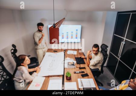 International architects, engineers and partners discuss blueprints, brainstorm projects and strategize in a diverse, collaborative boardroom. Stock Photo