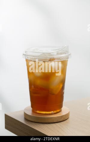 Iced tea in a plastic cup on a wooden table with a white background. Stock Photo
