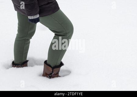 woman in winter clothes walks through deep snow. a foot in warm shoes steps into a snowdrift. foot falls in the snow. snowy winter. after snowfall Stock Photo