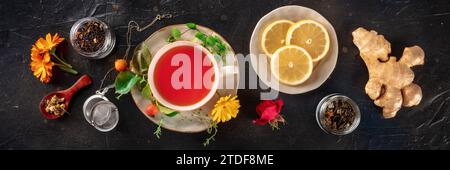 Tea with herbs, fruits, and flowers panorama, overhead flat lay shot on a black background. Healthy natural remedy Stock Photo