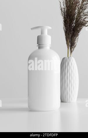 White cosmetic liquid soap dispenser bottle mockup with a dry flower on the white table. Stock Photo