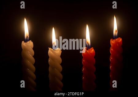 burning candle flame or light is glowing on four spiral candles on black or dark background on table in church for Christmas, funeral or memorial Stock Photo