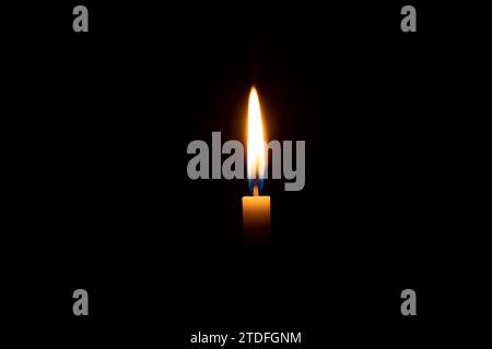 A single burning candle flame or light is glowing on an orange candle on black or dark background on table in church for Christmas, funeral Stock Photo