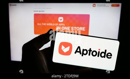 Person holding smartphone with logo of Portuguese app marketplace company Aptoide S.A. in front of website. Focus on phone display. Stock Photo